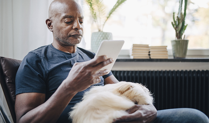 Man with a dog on his lap reading e-reader
